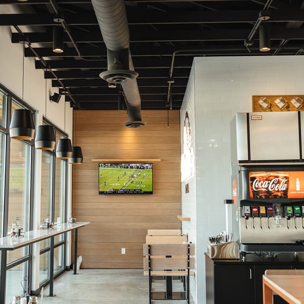 Modern Versalia Pizza interior with high-top seating, a TV showing football, and a soda fountain.