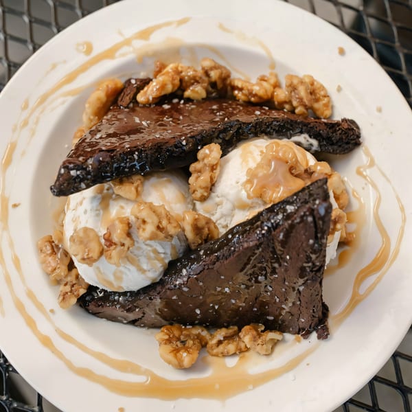 Versalia Pizza's brownie dessert with vanilla ice cream, walnuts, and caramel drizzle on a white plate.
