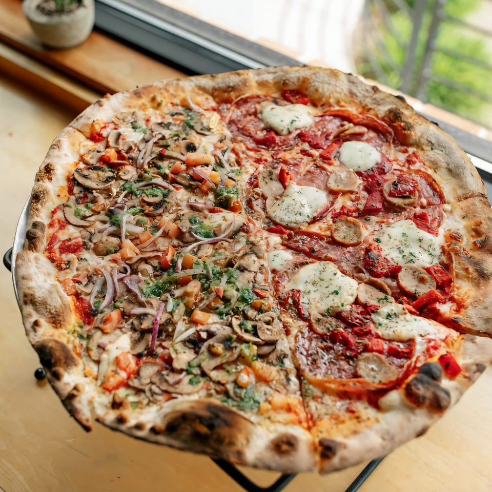 A large Versalia Pizza with two different halves, one with mushrooms and vegetables, the other with pepperoni and sausage.